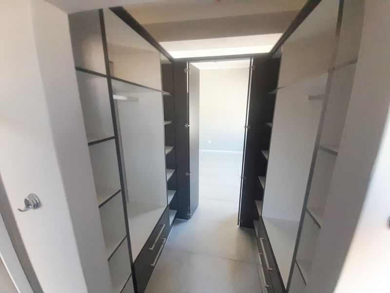 A walk-in dressing area featuring modern built-in cupboards with shelving and hanging space, finished with neutral floor tiles.