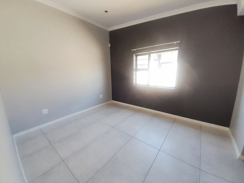 A bright, empty bedroom featuring neutral tiled flooring, a dark accent wall, and a window fitted with security burglar bars.