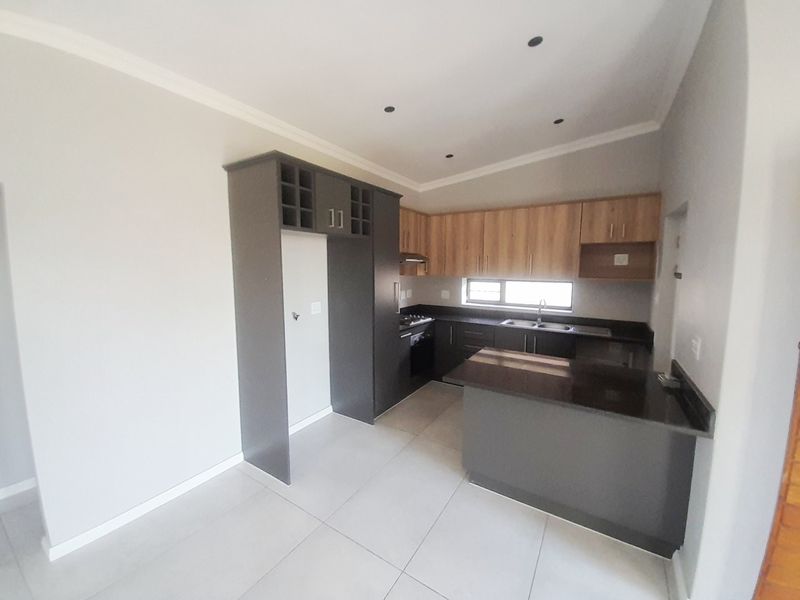 Modern kitchen featuring dark grey and wood-tone cabinetry, granite countertops, built-in oven and hob, and a functional breakfast nook with tiled flooring.