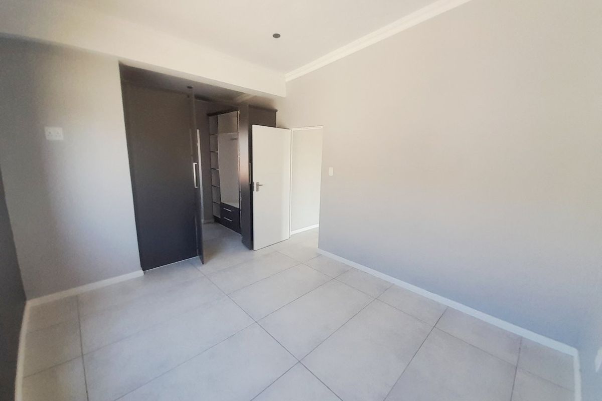 A clean, empty bedroom featuring neutral tiled flooring, built-in cupboards, and modern finishes, ready for personalization.
