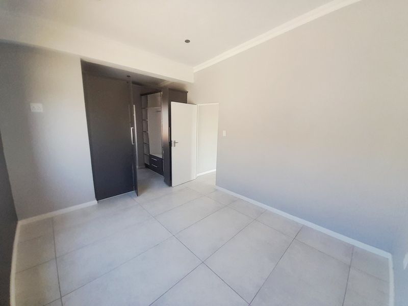 A clean, empty bedroom featuring neutral tiled flooring, built-in cupboards, and modern finishes, ready for personalization.