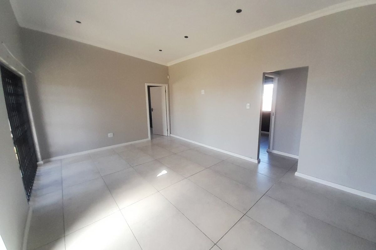 A bright, empty living area featuring neutral walls, large format floor tiles, recessed downlighting, and a secure entrance gate.