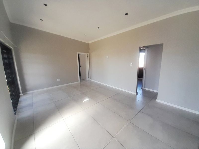 A bright, empty living area featuring neutral walls, large format floor tiles, recessed downlighting, and a secure entrance gate.