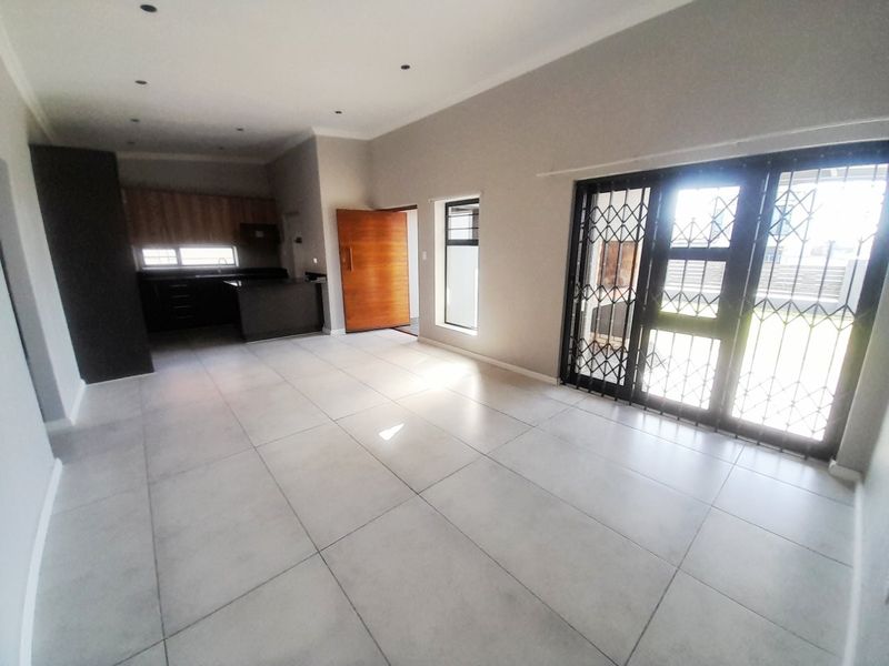 Spacious open-plan living area featuring modern tiled flooring, recessed lighting, and a sleek kitchen with built-in cabinetry, leading to an outdoor patio area.