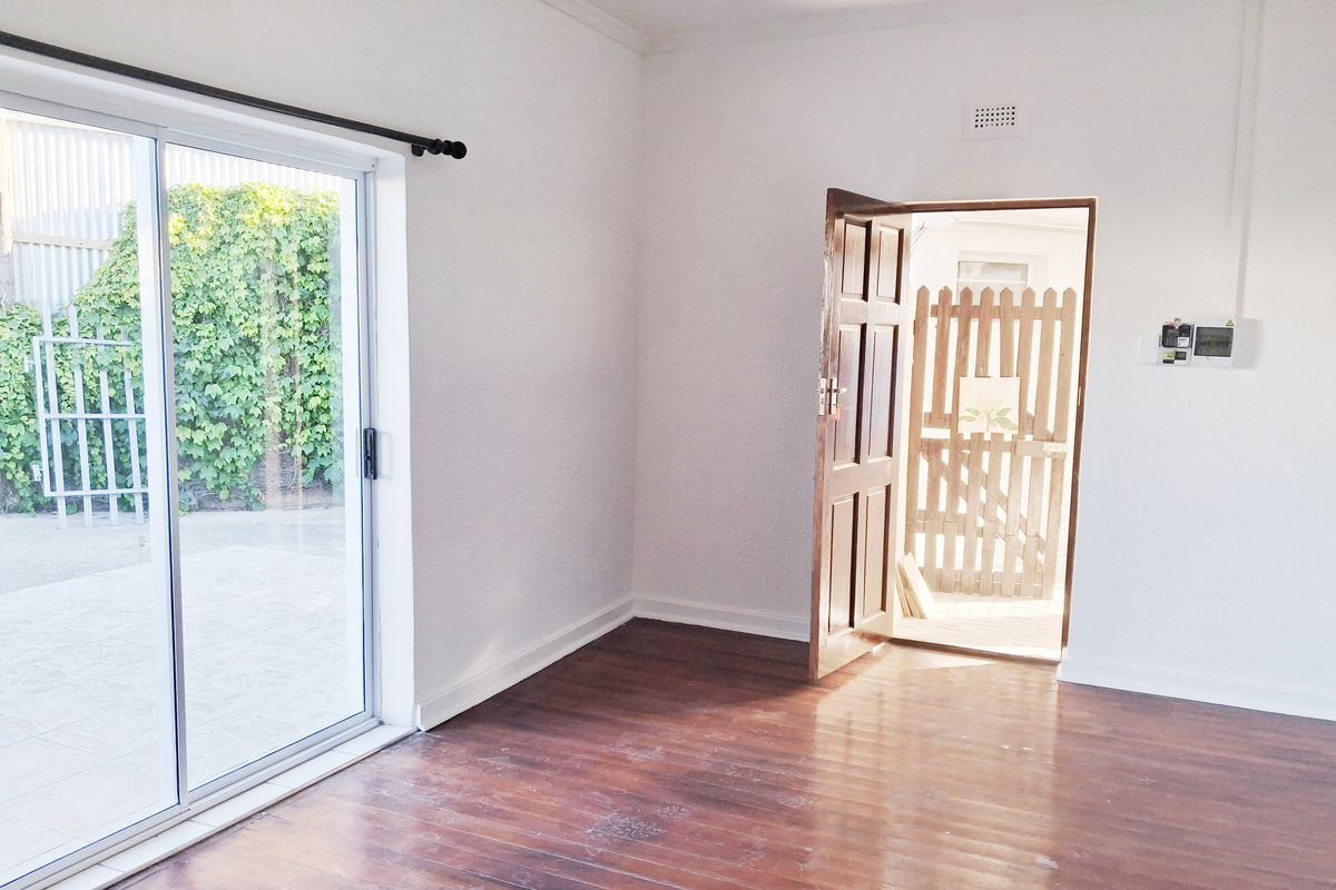 An empty living room featuring polished timber flooring, a sliding glass door leading to the exterior, and a secure entrance door.