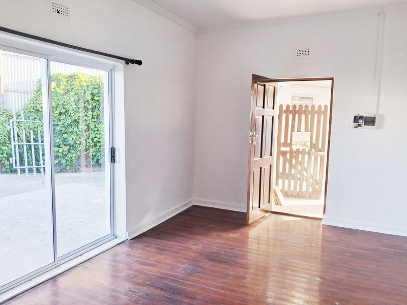 An empty living room featuring polished timber flooring, a sliding glass door leading to the exterior, and a secure entrance door.