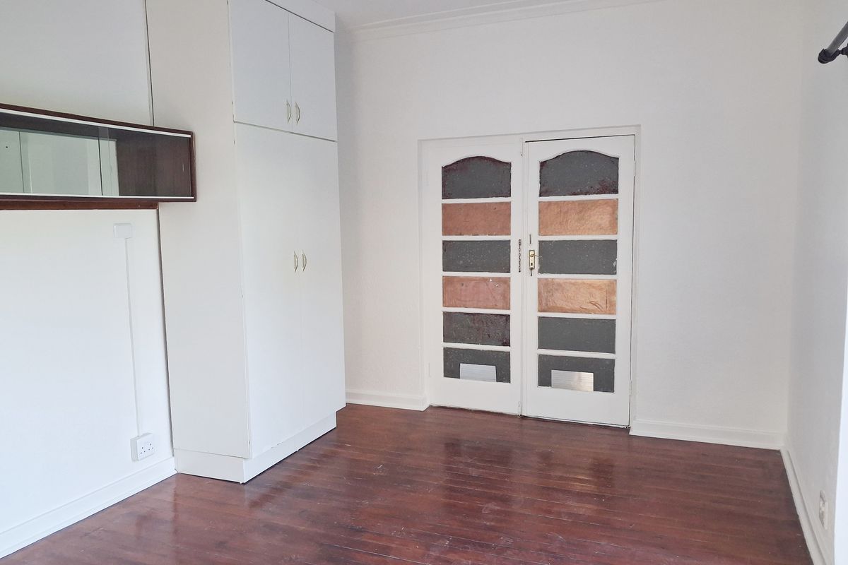 An empty bedroom featuring original timber flooring, a built-in white cupboard, and classic double doors with decorative glass panels.