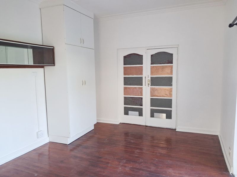An empty bedroom featuring original timber flooring, a built-in white cupboard, and classic double doors with decorative glass panels.