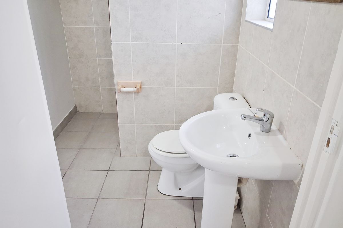 A functional bathroom featuring a pedestal washbasin, toilet, and neutral ceramic tiling throughout.