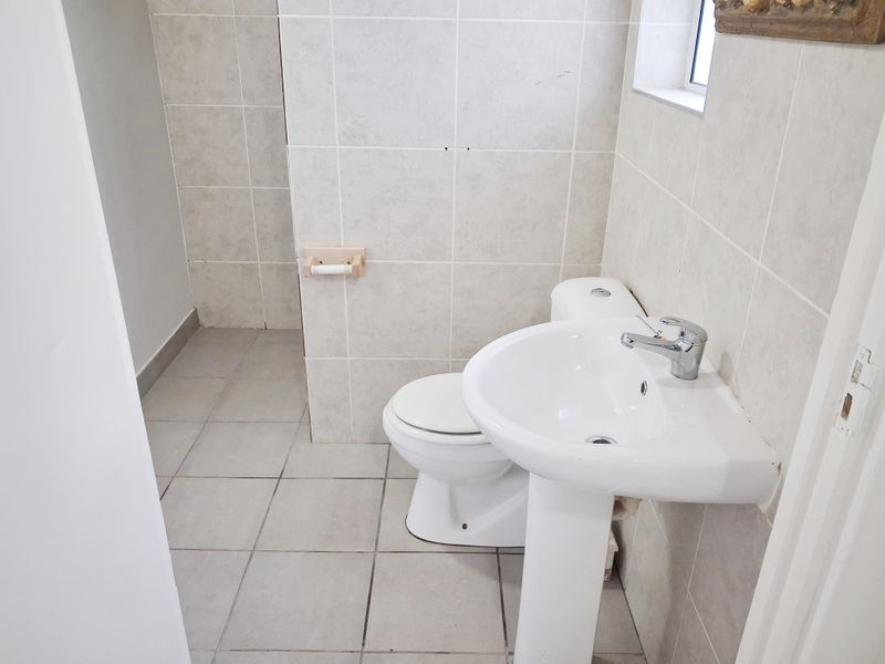 A functional bathroom featuring a pedestal washbasin, toilet, and neutral ceramic tiling throughout.