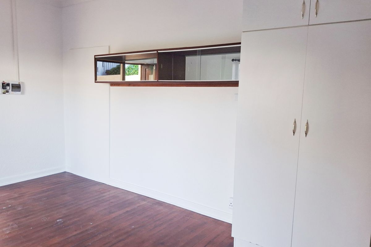 A vacant bedroom featuring wooden flooring, built-in white cupboards, and a wall-mounted mirror cabinet, offering a clean canvas for personalization.