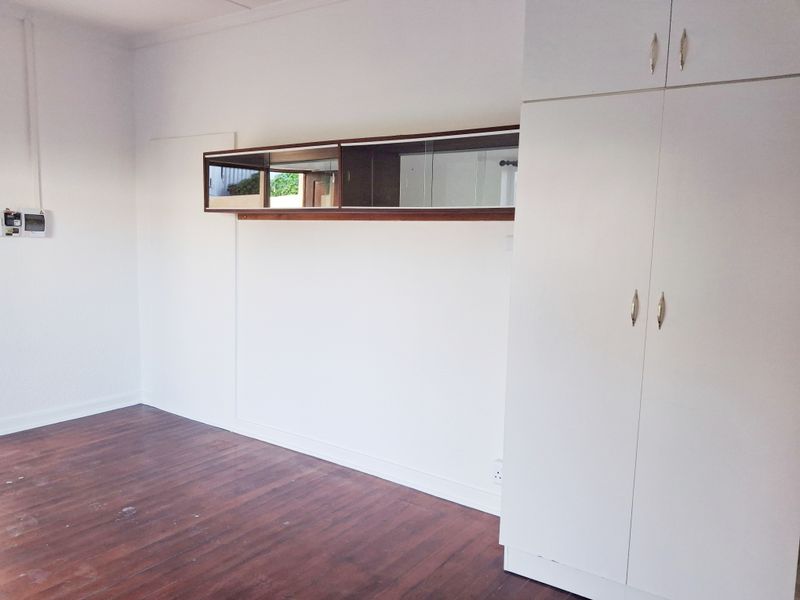 A vacant bedroom featuring wooden flooring, built-in white cupboards, and a wall-mounted mirror cabinet, offering a clean canvas for personalization.