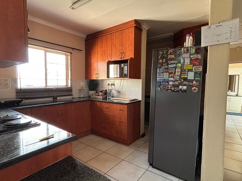 A functional kitchen featuring warm-toned wooden cabinetry, granite countertops, and tiled flooring, offering a practical layout with integrated appliance space.
