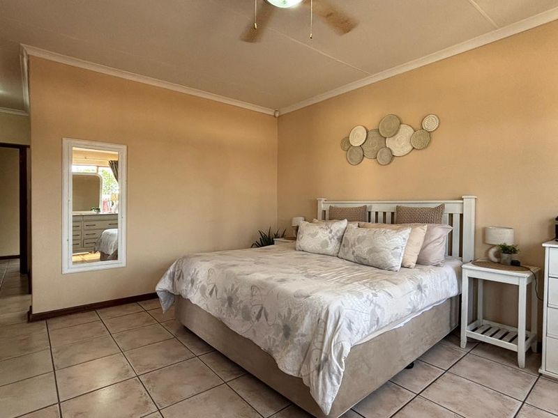 Spacious bedroom featuring neutral wall tones, tiled flooring, a ceiling fan, and built-in storage cupboards.
