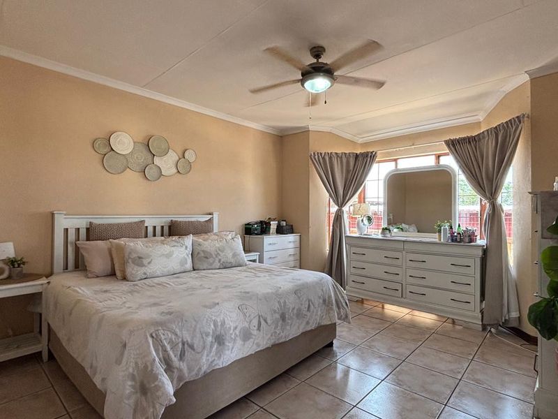 Spacious bedroom featuring tiled flooring, a central ceiling fan, and large windows allowing for natural light.