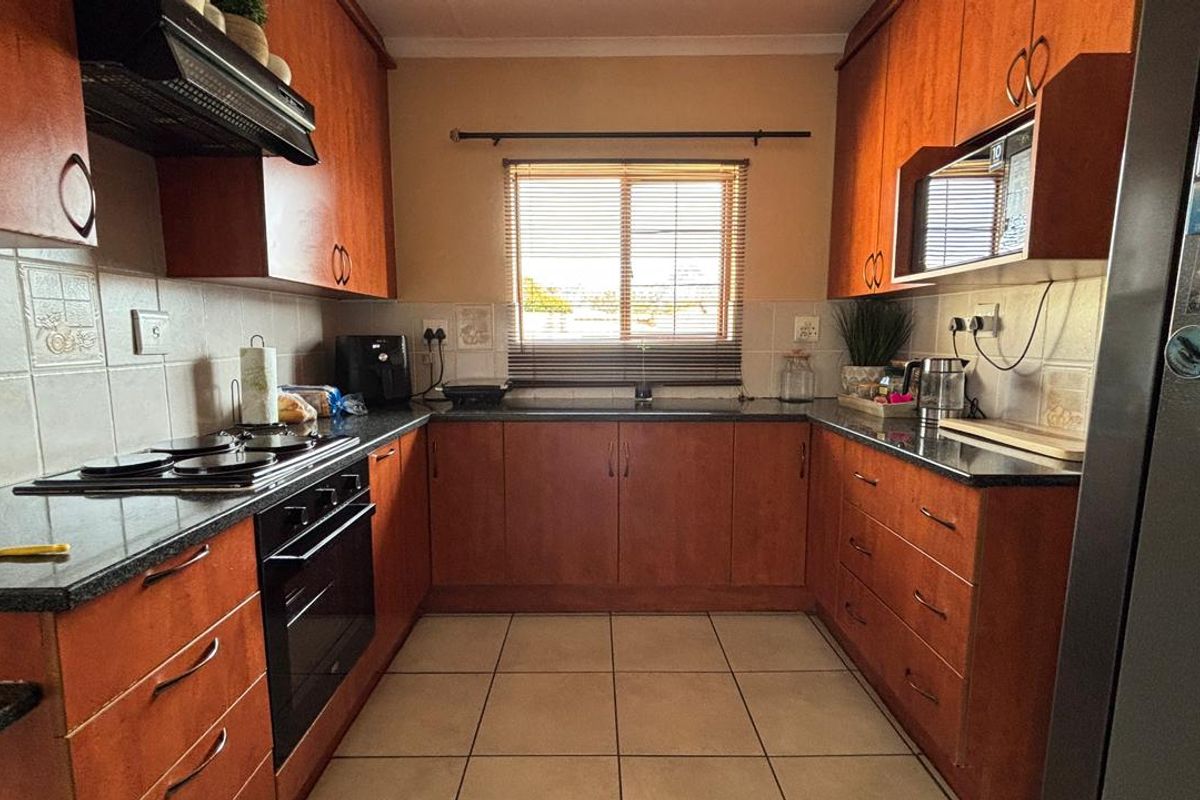 A functional U-shaped kitchen featuring warm-toned wooden cabinetry, granite countertops, a built-in oven, electric hob, and tiled flooring.