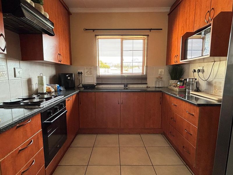 A functional U-shaped kitchen featuring warm-toned wooden cabinetry, granite countertops, a built-in oven, electric hob, and tiled flooring.