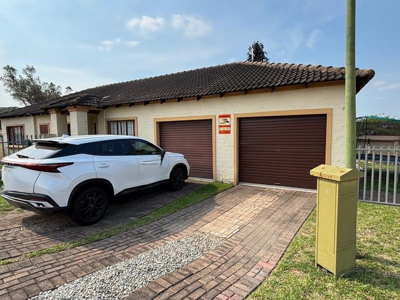 Front exterior view of a single-story house featuring a double garage, paved driveway, and perimeter security fencing.