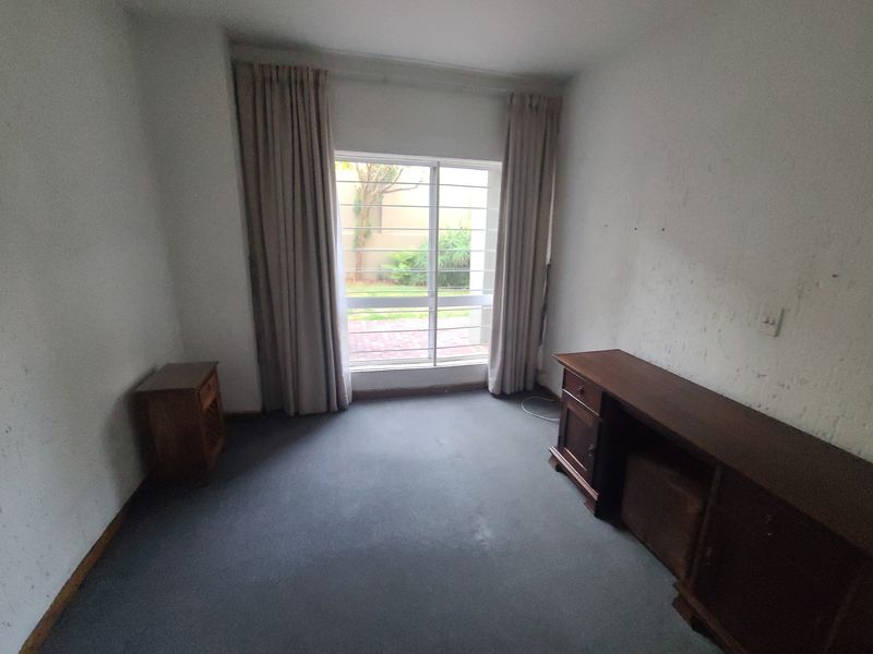 A bedroom featuring carpet flooring, security bars on the window, and curtain tracks, requiring wall repairs and repainting to improve its condition.