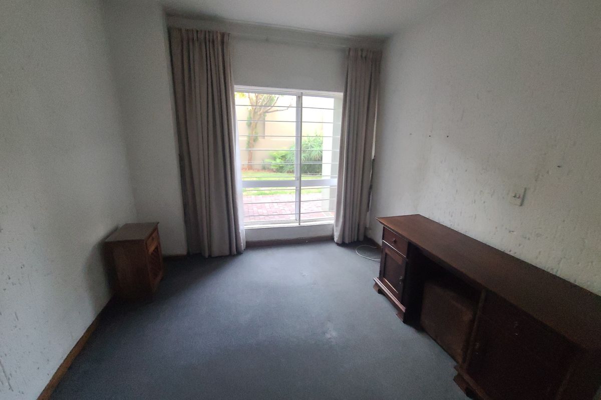 A bedroom featuring carpet flooring, security bars on the window, and curtain tracks, requiring wall repairs and repainting to improve its condition.