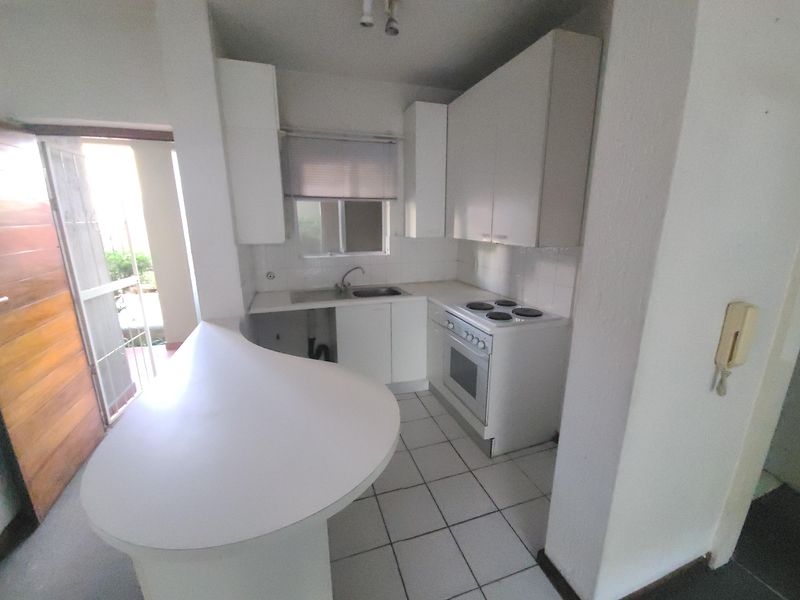 Compact kitchen featuring white cabinetry, an electric stove, and a breakfast bar, requiring minor repairs to cabinetry and plumbing fixtures.