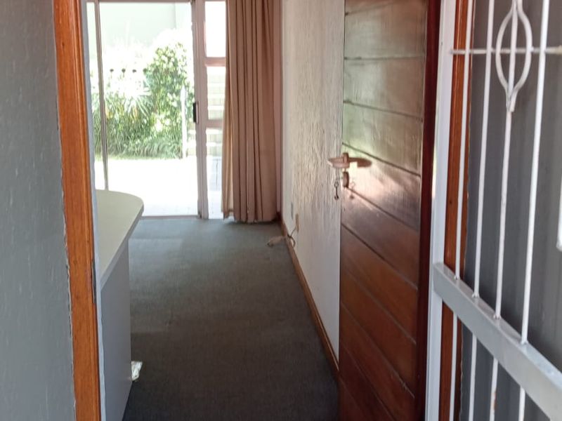 View through the apartment entrance featuring a security gate, timber door, and carpeted hallway leading to a sliding glass door.