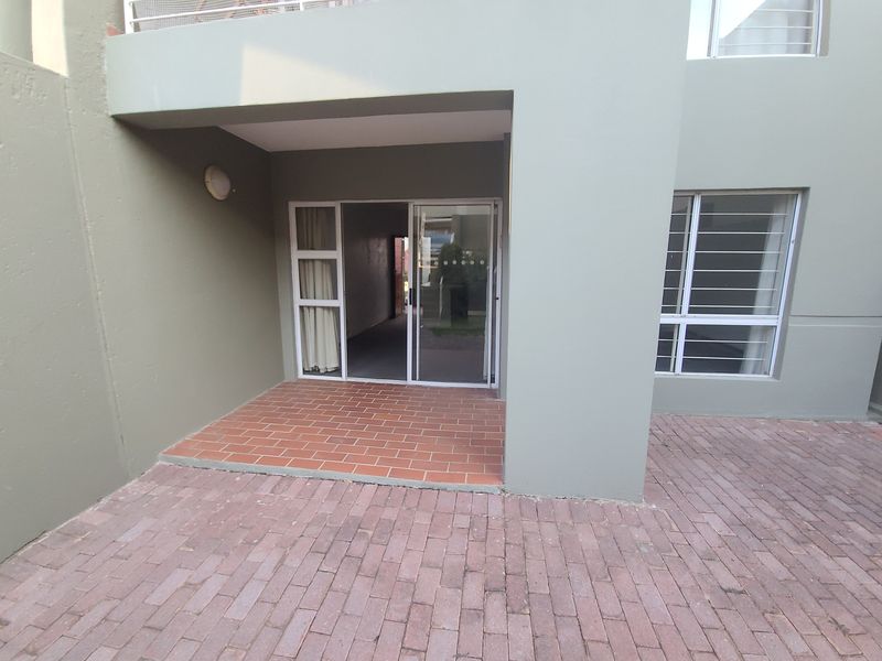 A paved ground-floor patio area featuring a sliding glass door entrance with security bars and exterior wall lighting.