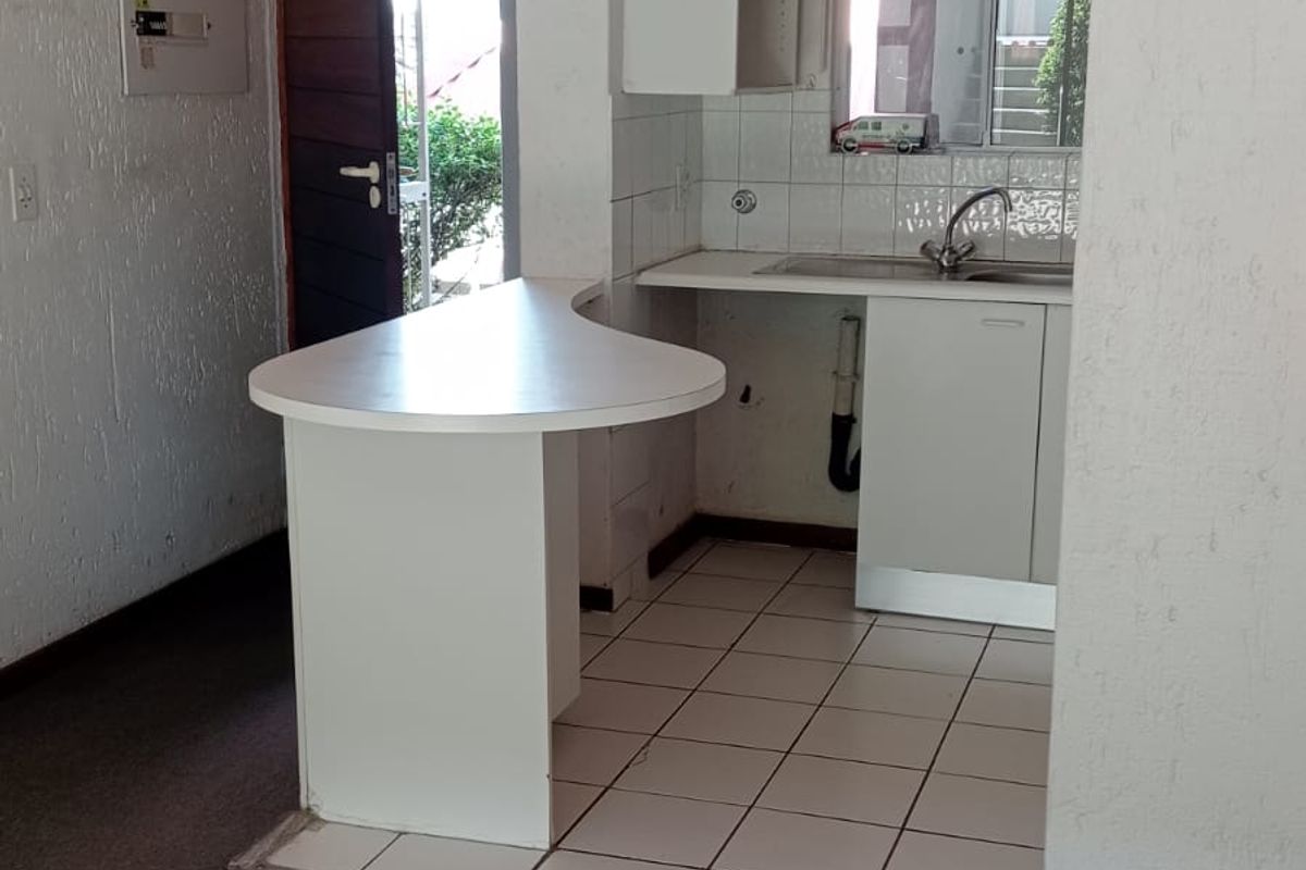 A compact kitchen area featuring built-in cabinetry, a breakfast bar, and tiled flooring, currently vacant and ready for modernization.
