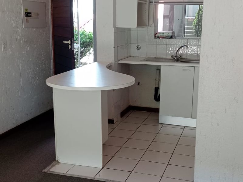 A compact kitchen area featuring built-in cabinetry, a breakfast bar, and tiled flooring, currently vacant and ready for modernization.