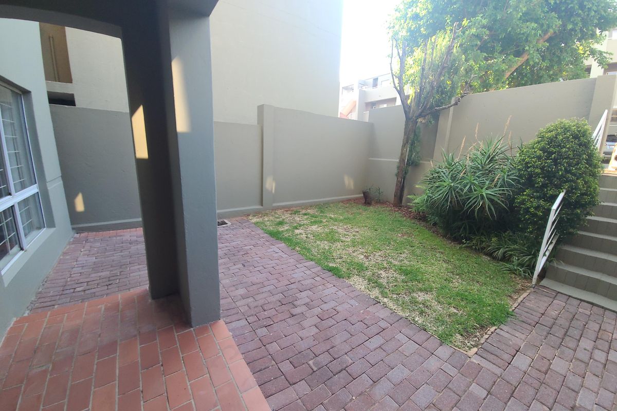 A private rear courtyard featuring a paved patio area, a small lawn, and a concrete staircase leading to an upper level.
