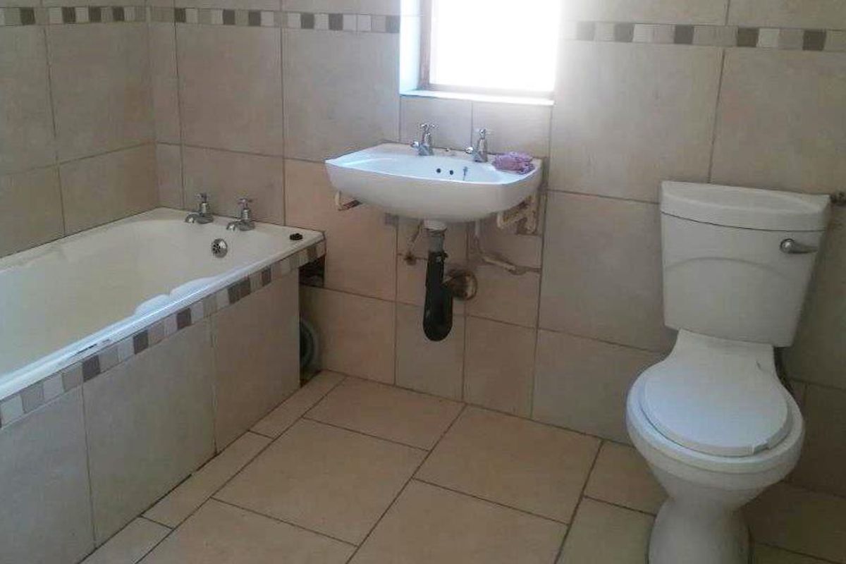 A functional bathroom featuring a standard bathtub, wall-mounted basin, and toilet with neutral tiled walls and flooring.