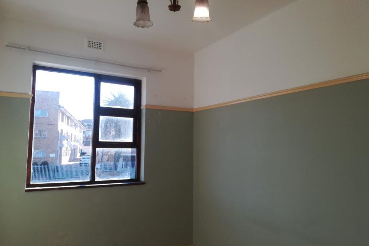 A bright, empty bedroom featuring two-tone wall paint, a classic ceiling light fixture, and a large window overlooking the street.