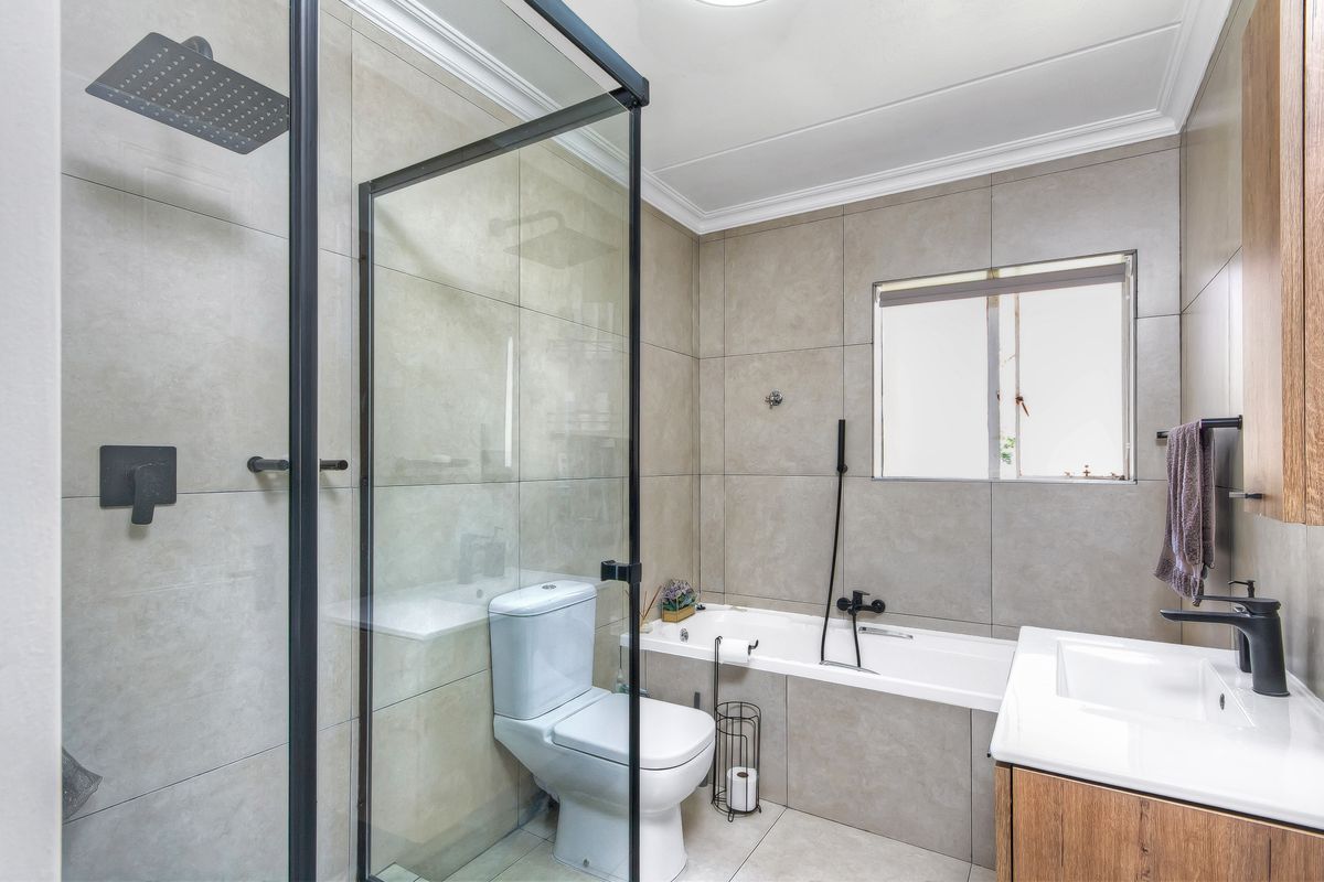 Modern bathroom featuring a glass-enclosed shower, a built-in bathtub, a vanity with a basin, and contemporary matte black fixtures.