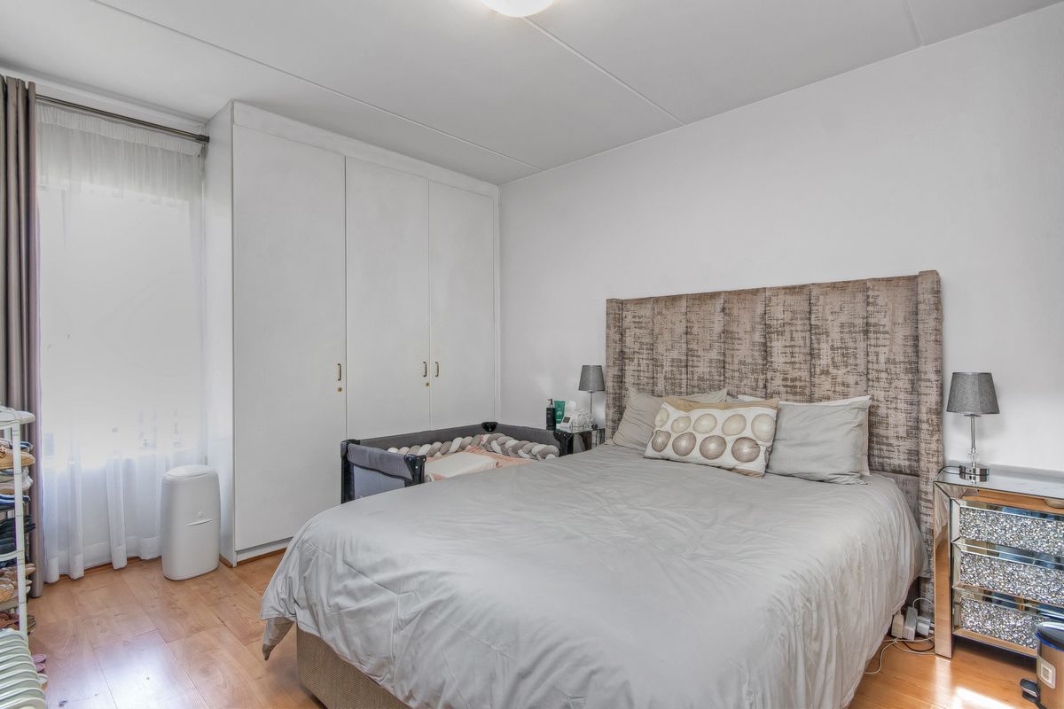A bedroom featuring built-in floor-to-ceiling wardrobes and light-toned laminate flooring.