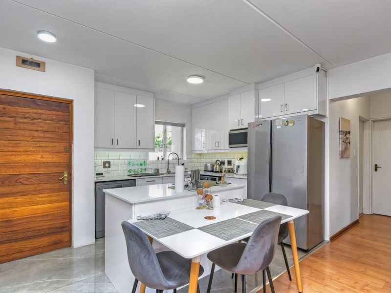 A modern open-plan kitchen featuring white cabinetry, stone countertops, a subway tile backsplash, and an integrated breakfast bar area.