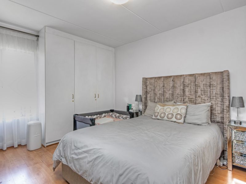 A bedroom featuring built-in floor-to-ceiling wardrobes and light-toned laminate flooring.