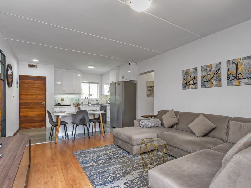 An open-plan living and kitchen area featuring wood-look flooring, white cabinetry, subway tile backsplash, and a functional layout suitable for modern apartment living.