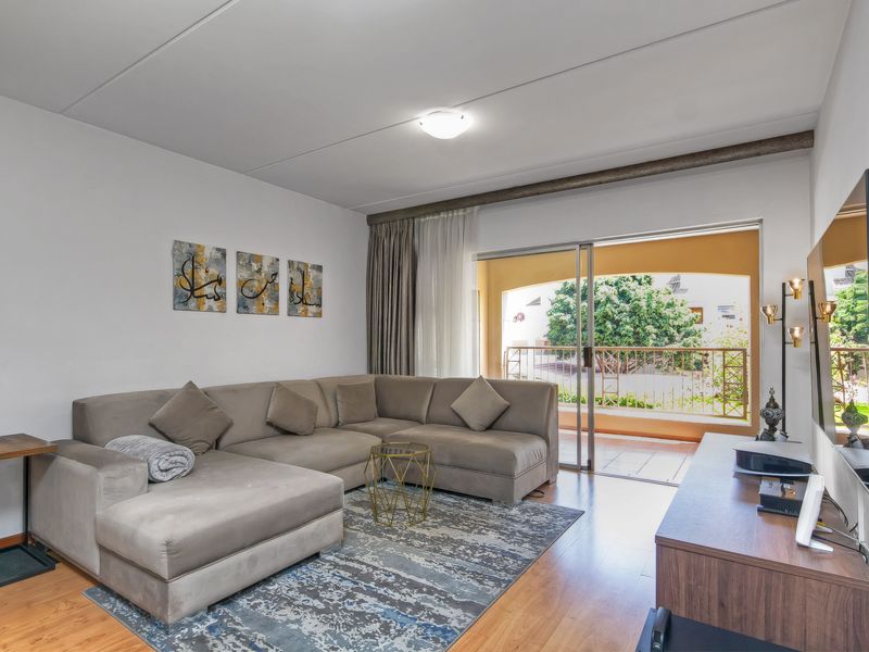 A bright living room featuring laminate flooring and large sliding glass doors that open onto a private balcony.