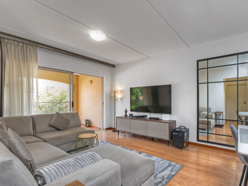 A bright living room featuring laminate flooring, a large sliding door leading to a private balcony, and a full-length decorative wall mirror.