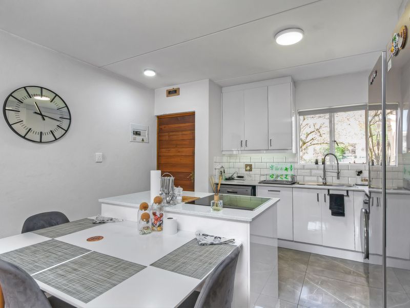 Modern open-plan kitchen featuring white cabinetry, stone countertops, subway tile backsplash, and integrated sink, seamlessly flowing into the dining area.