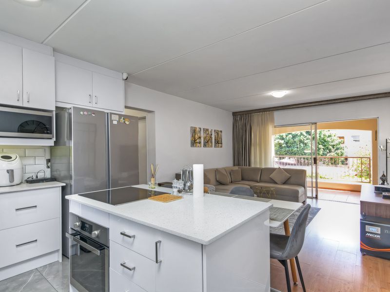 Open-plan living area featuring a modern kitchen with white cabinetry, stone countertops, built-in oven and hob, flowing into a lounge with balcony access.