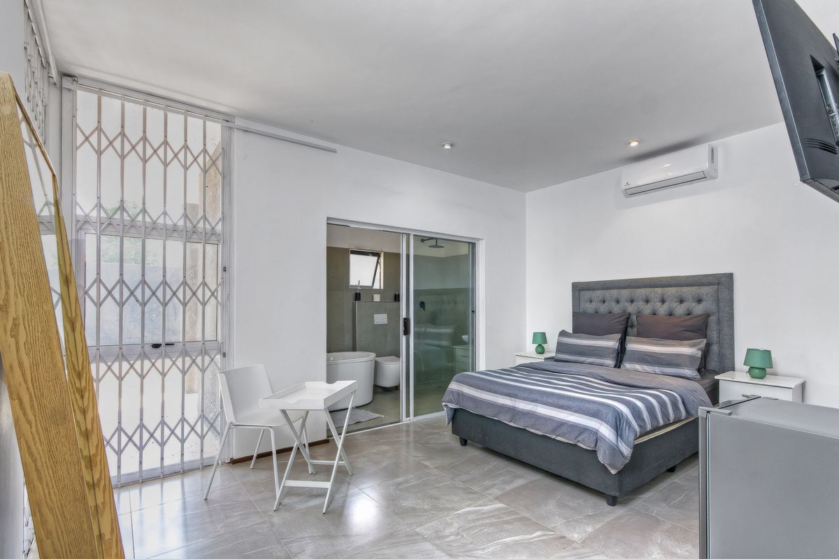 A modern bedroom featuring tiled flooring, an en-suite bathroom with glass sliding doors, and a wall-mounted air conditioning unit.