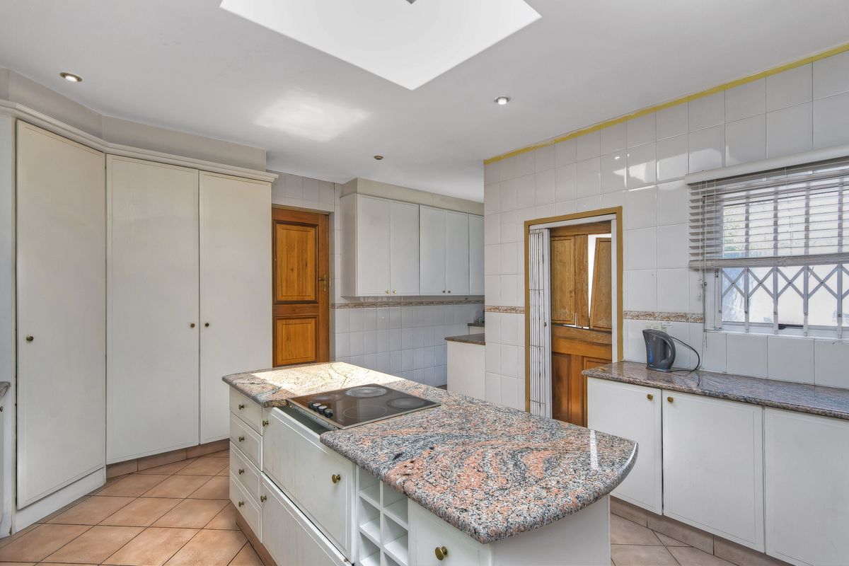 A functional kitchen featuring a central island with a built-in electric hob, granite countertops, ample cabinetry, and a skylight providing natural illumination.