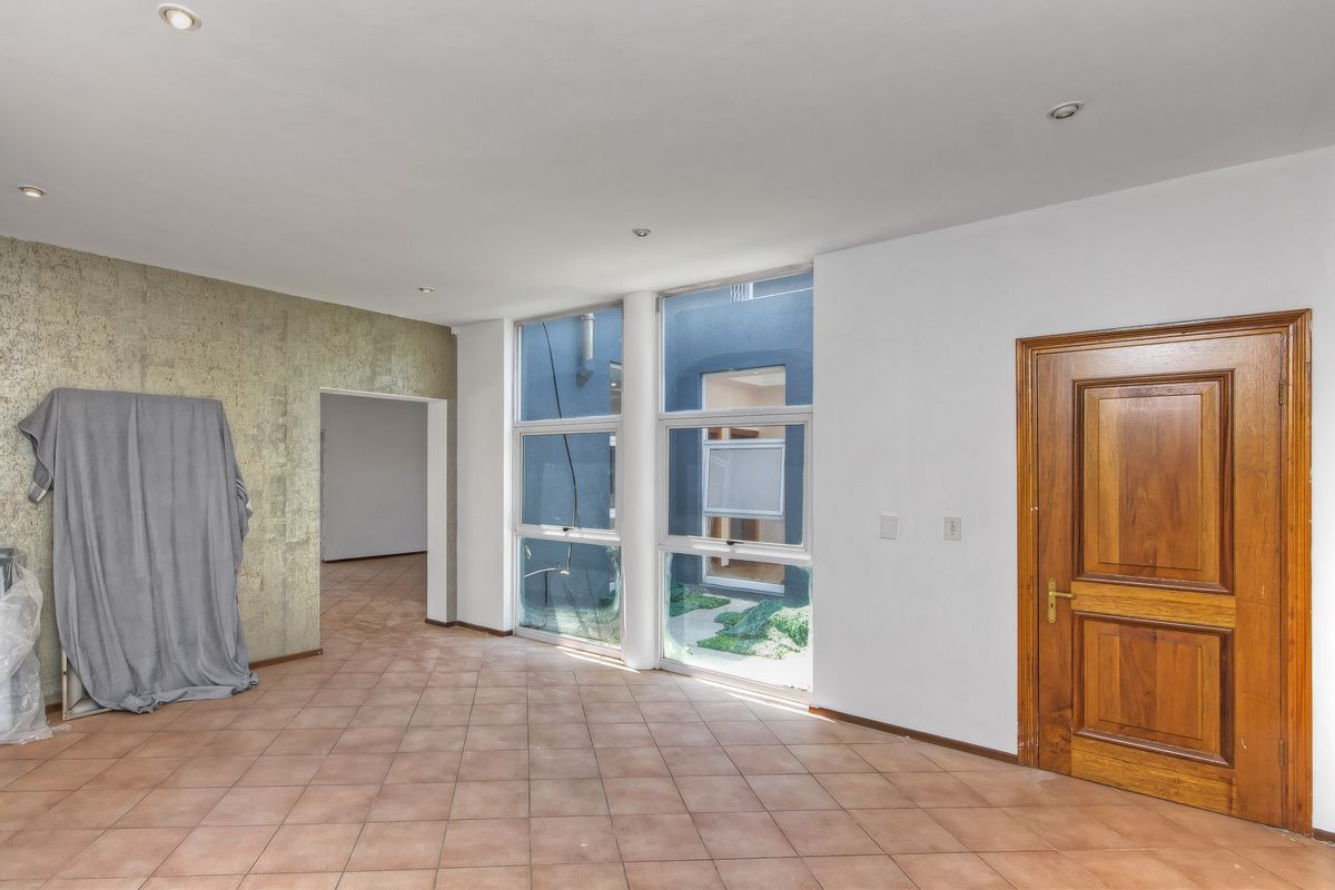 An empty living area featuring large windows overlooking a courtyard, tiled flooring, recessed ceiling lighting, and a solid timber door.