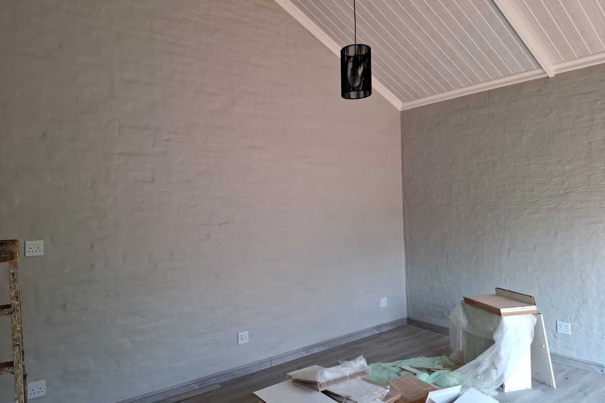 A bright living area featuring textured painted brick walls, vaulted timber-paneled ceilings, and modern laminate flooring.