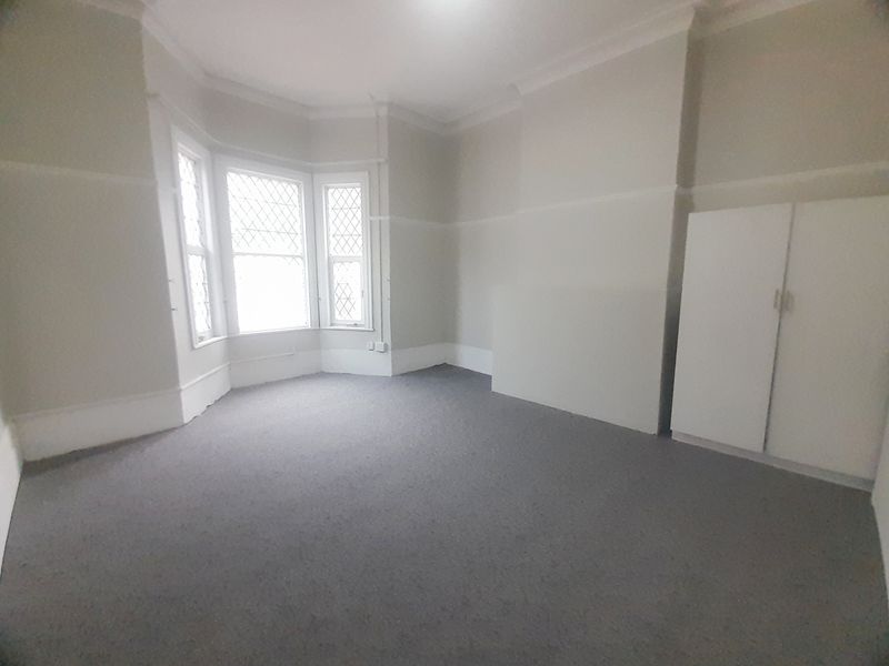 Spacious bedroom featuring a classic bay window with leaded glass detailing, neutral wall finishes, and a built-in wardrobe.