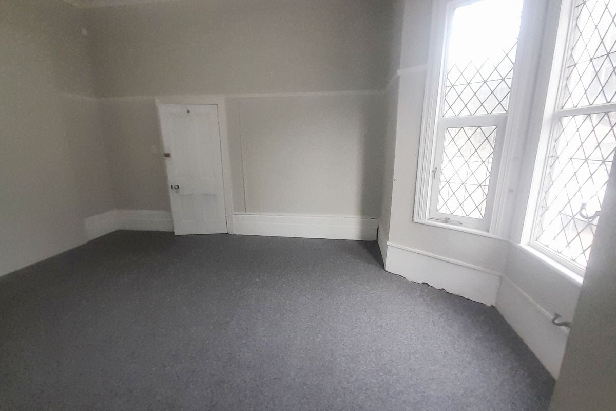 An empty bedroom featuring a characterful leaded glass bay window, neutral walls, picture rails, and grey carpet flooring.