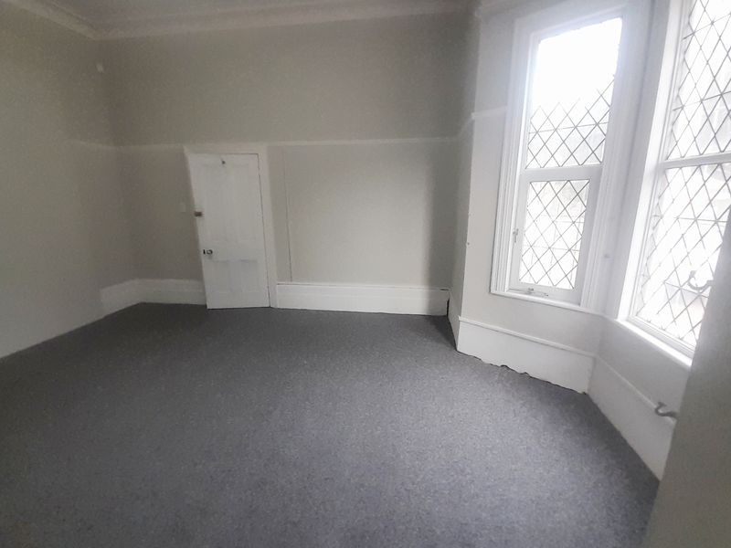 An empty bedroom featuring a characterful leaded glass bay window, neutral walls, picture rails, and grey carpet flooring.