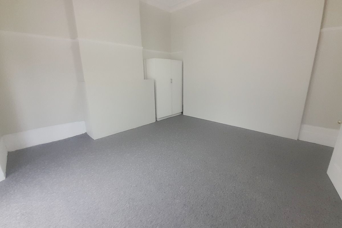 A clean, empty bedroom featuring neutral walls, grey carpeting, and a built-in cupboard, providing a versatile space ready for personalization.