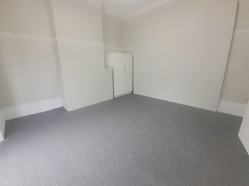 A clean, empty bedroom featuring neutral walls, grey carpeting, and a built-in cupboard, providing a versatile space ready for personalization.
